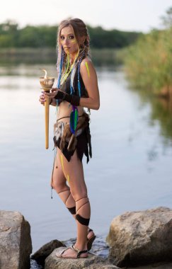 Elinde yanan bir meşale olan amazon kadın, ortaçağ kürk kostümü giyiyor, nehrin arka planında..