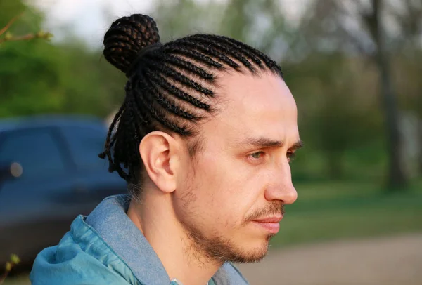 profile of a guy with a cornrows hairstyle, collected in the tail, portrait, close-up