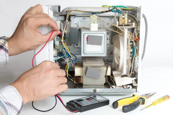 Repair of a microwave oven. The master measures the voltage with a tester, on a white isolated background