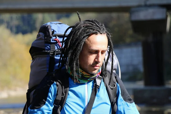 a tourist with dreadlocks and a hiking backpack on his back crosses a mountain river into a ford