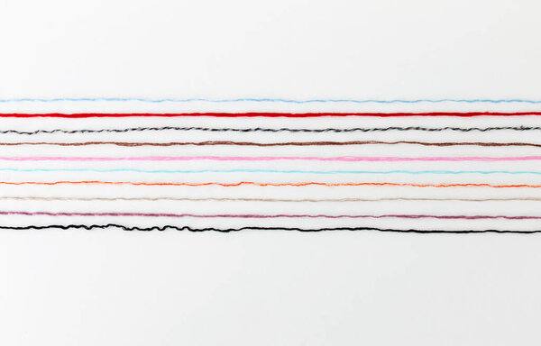 multi-colored threads of yarn laid out on a white background, close-up