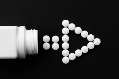 Tıbbi haplar, izole edilmiş karanlık bir arka planda, bir kutu hapın yanında ok şeklinde serilmişti.