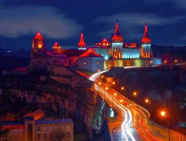 Scenic nightscape of illuminated medieval fortress of Kamianets-Podilskyi, Ukraine. Picturesque moving clouds in night sky