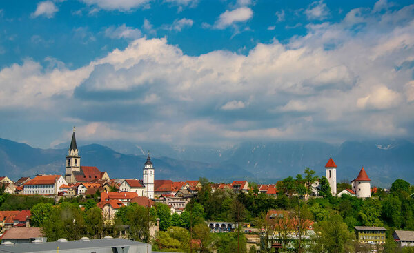 Panoramic view of old churches, castle tower and historical city center of Kranj, Slovenia with mountains covered by clouds on background
