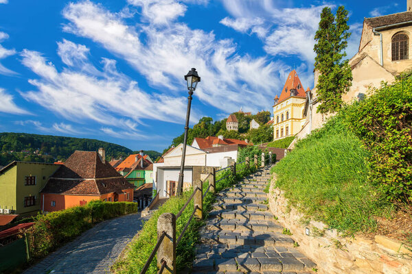 Stone paved alley on hillside to medieval fortified city of Sighisoara, Transylvania region, Romania. Birthplace of Vlad Dracula. UNESCO world heritage site. Picturesque sky