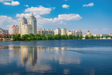 Residential buildings on the bank of Dnieper river reflected in the water at sunny summer day. Obolon district, Kyiv, Ukraine.
