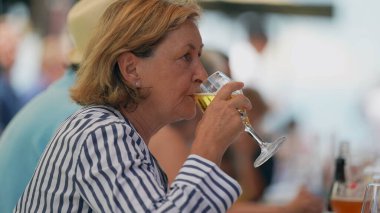 Restoranda oturmuş cam bira içen yaşlı bir kadın. Yaşlı bayan bir yudum serinletici içecek alır.