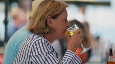 Restoranda oturmuş cam bira içen yaşlı bir kadın. Yaşlı bayan bir yudum serinletici içecek alır.