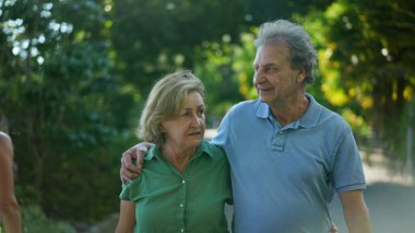 Güneşli bir günde yürüyen düşünceli yaşlı çift, 60 'lı yaşlarda