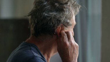 Yaşlı adam kulak tırmalayan kulak memesine dokunuyor.