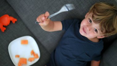 Mutlu çocuk kanepede oturmuş kameraya bakarak kavun yiyor.