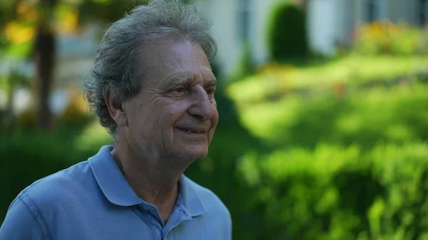 Smiling senior man walking outside in green path, one happy older person