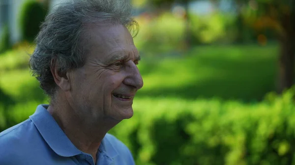 Smiling senior man walking outside in green path, one happy older person