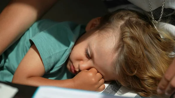 Sleepy child rubbing eye with hand, kid lying down resting