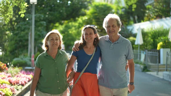Senior parents walking together with adult daughter outside talking in conversation