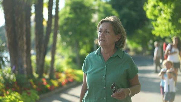 Older woman walking outdoors in green urban city, senior person walks forward outside