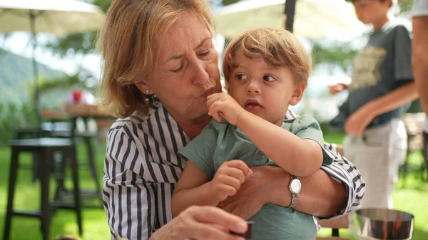 Grand-mother holding toddler grand-son in arms outside. candid and real life
