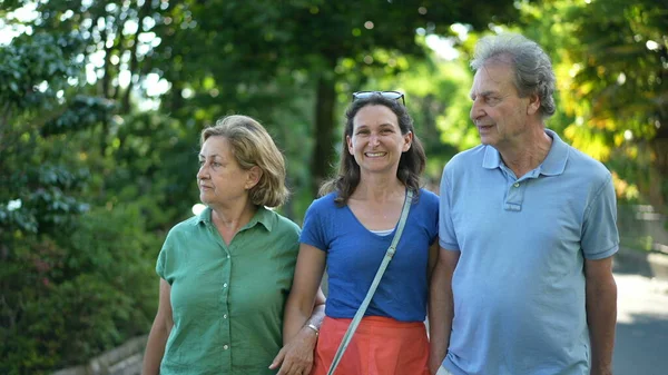 Family walking together in green city, happy adult daughter with senior parents