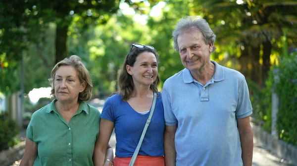 Family walking together in green city, happy adult daughter with senior parents