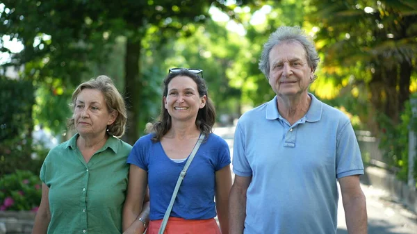 Family walking together in green city, happy adult daughter with senior parents