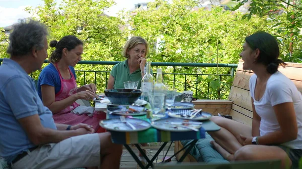 Family sitting at table during lunch outside in conversation during summer day