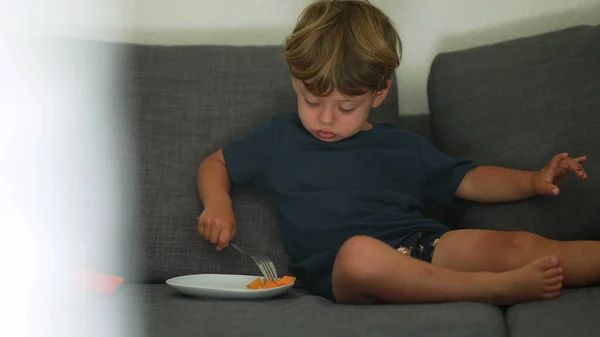 Child eating melon fruit snack sitting on sofa at home