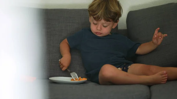 Child eating melon fruit snack sitting on sofa at home