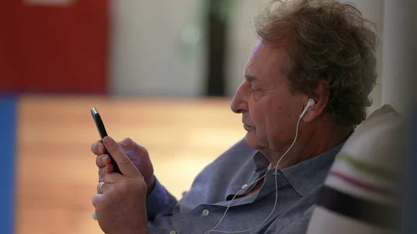 Candid pensive senior person using phone wearing earphones