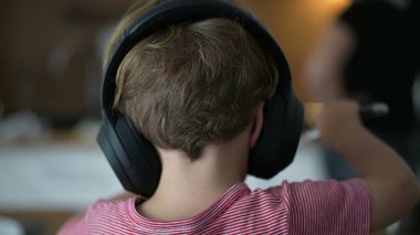 Back of child wearing headphones listening to audio