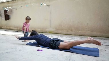 Baba, yanında yeni yürümeye başlayan oğluyla dışarıda egzersiz yapıyor.