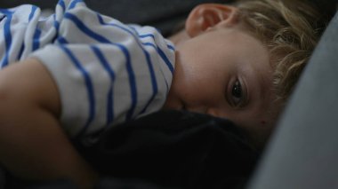 Uykulu küçük çocuk kanepeye uzanıp uyumaya hazırlanıyor.