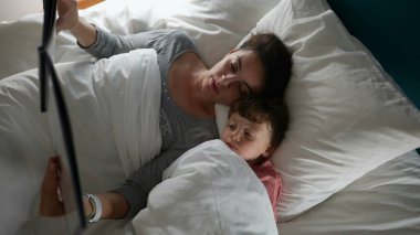 Anne uyumadan önce yatağında çocuğa masal okuyor.