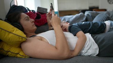 Annem kanepeye uzanmış, çocuğu karnında uyurken cep telefonu kullanıyor.