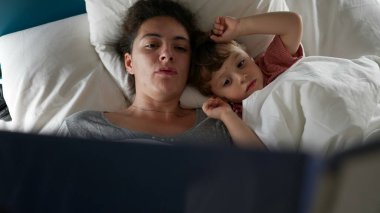 Anne uyumadan önce çocuk ile yatakta uzanıp masal okuyor.