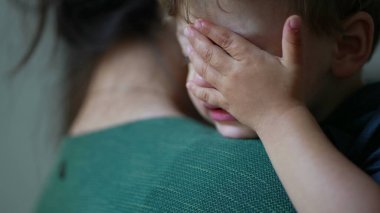 Anne kucağında ağlayan küçük çocuk gözyaşlarını siliyor.