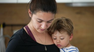 Anne kucağında bebekle yemek pişiriyor.