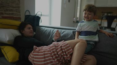 Anne ve küçük çocuk evdeki kanepede rahat ve gerçek hayatta oturuyor.