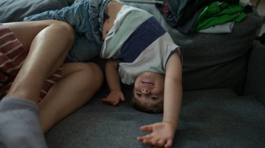 Küçük çocuk evdeki kanepede baş aşağı oyun oynuyor.