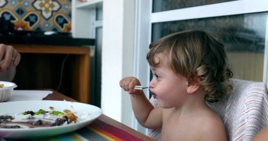 Küçük çocuk kaşıkla öğle yemeği yiyor. Küçük bebek kendi başına yemek yiyor.