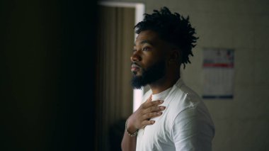 Düşünceli genç bir siyah adam pencerenin kenarında durup hayatı düşünüyor.