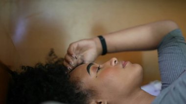 Düşünceli bir kadın yatakta, saçlarıyla oynuyor.