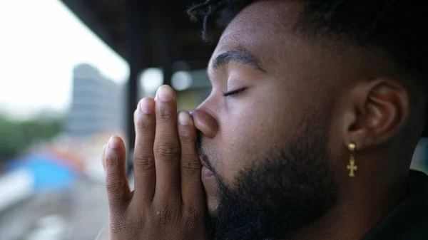 A young black man praying to God person opening eyes to sky smiling