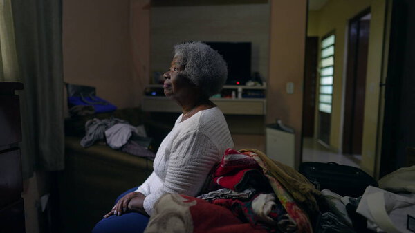 Созерцательная пожилая черная женщина, сидящая у спальни и выглядывающая в окно