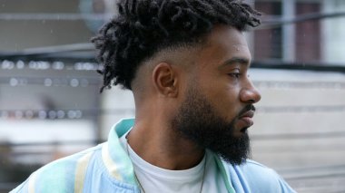 Düşünceli bir siyah adam çiseleyen çiselemede duruyor ve genç birinin profilini düşünüyor.