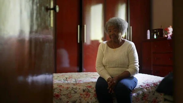 One senior black woman sitting by bedside in bedroom