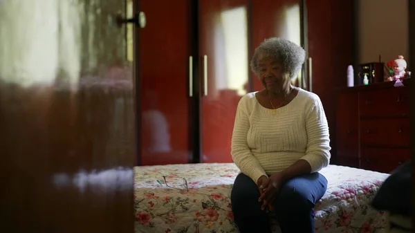 One senior black woman sitting by bedside in bedroom