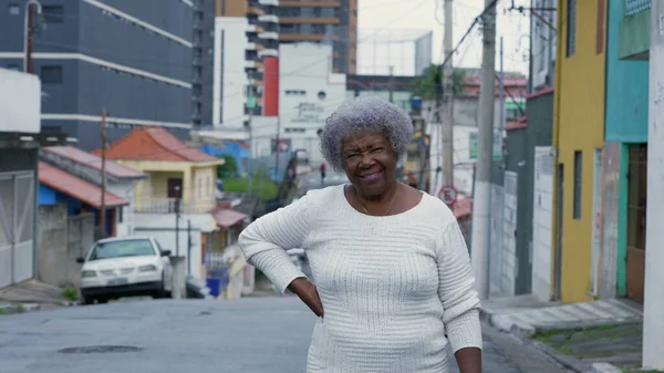 An older black woman standing outside in urban street looking at camera