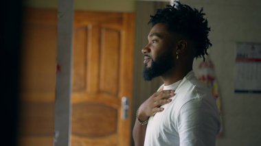 Genç siyah adam kameraya dönüp gülümsüyor. Pencereden dışarı bakıyor.