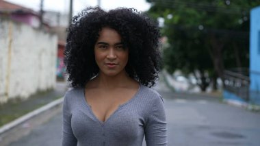 Dışarıda kameraya bakan kendine güvenen siyah bir kadın.