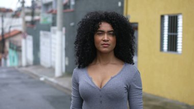 Dışarıda kameraya bakan kendine güvenen siyah bir kadın.